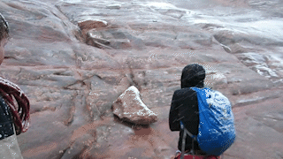 Animated GIF showing a snowy canyon in Utah. The camera zooms in to a man sitting on a ledge of rock waiting for rescue.